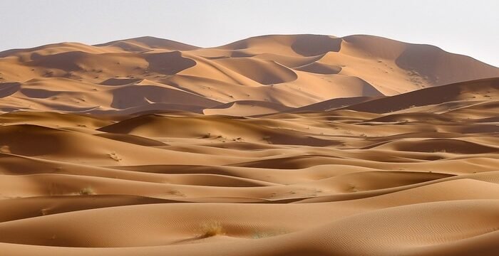Dunas alaranjadas do deserto de Merzouga sob céu azul.